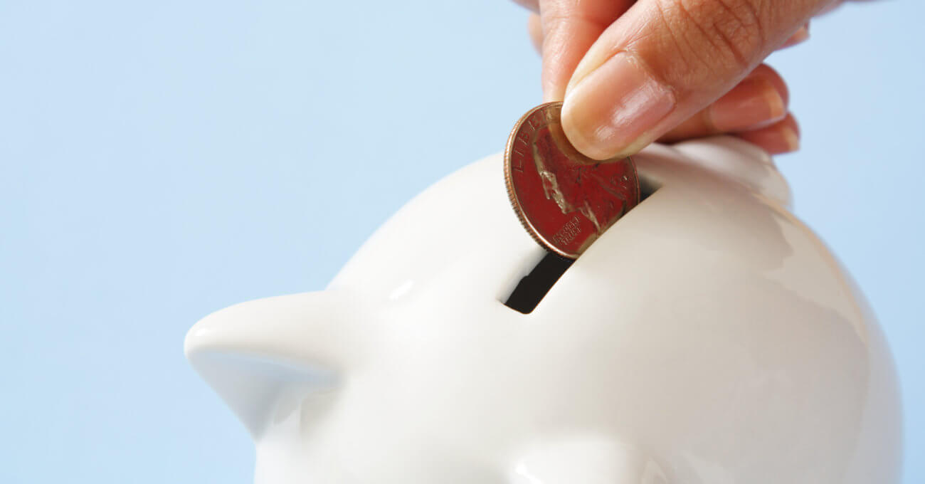 A woman is putting a quarter into a white piggy bank. The idea is that she is saving for college.