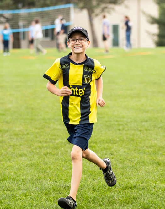 A young boy in a yellow and black shirt is joyfully running outdoors.